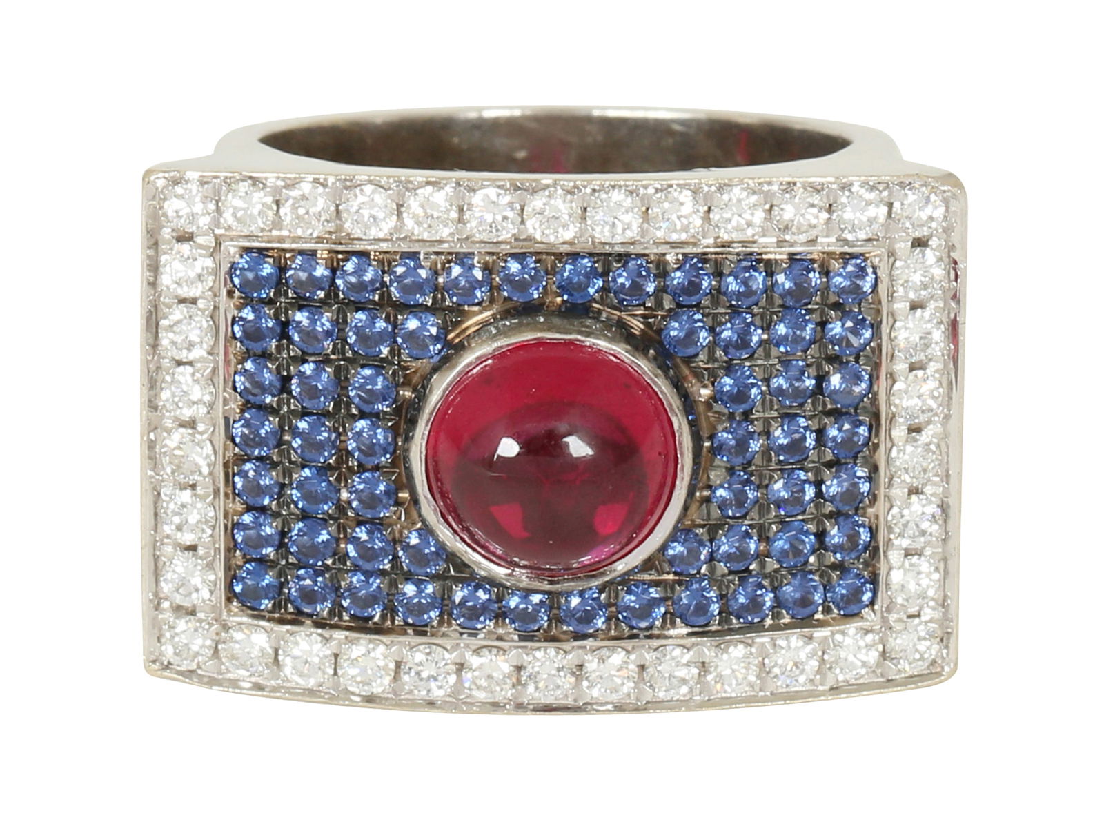 14K WHITE GOLD RING: Rectangular, convex element set with diamonds and blue stones, with a cabochon ruby in the center. Size approx. 8.5 US. Weight approx. 18.5 grams.