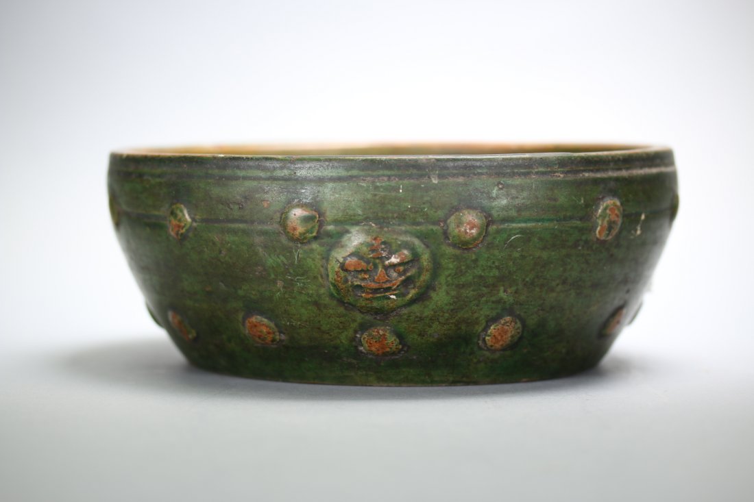 A Chinese green glazed pottery bowl,Han Dynasty: A Chinese green glazed pottery bowl,Han Dynasty. circular form with moulded bosses to body. Inscribed with lion faces on the outer surface. Size: 8 inches diameter.