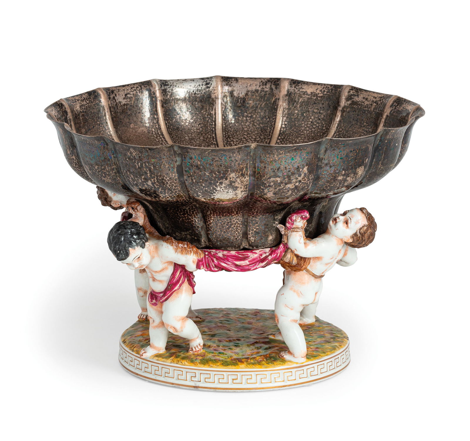CENTROTAVOLA IN PORCELLANA ED ARGENTO, ITALIA, XX: SECOLO su base circolare, quattro putti in porcellana di Capodimonte reggono una grande coppa in argento, punzonata Miracoli di Milano; difetti Alt. cm 25, larg. cm 36 AN ITALIAN PORCELAIN AND SILVER