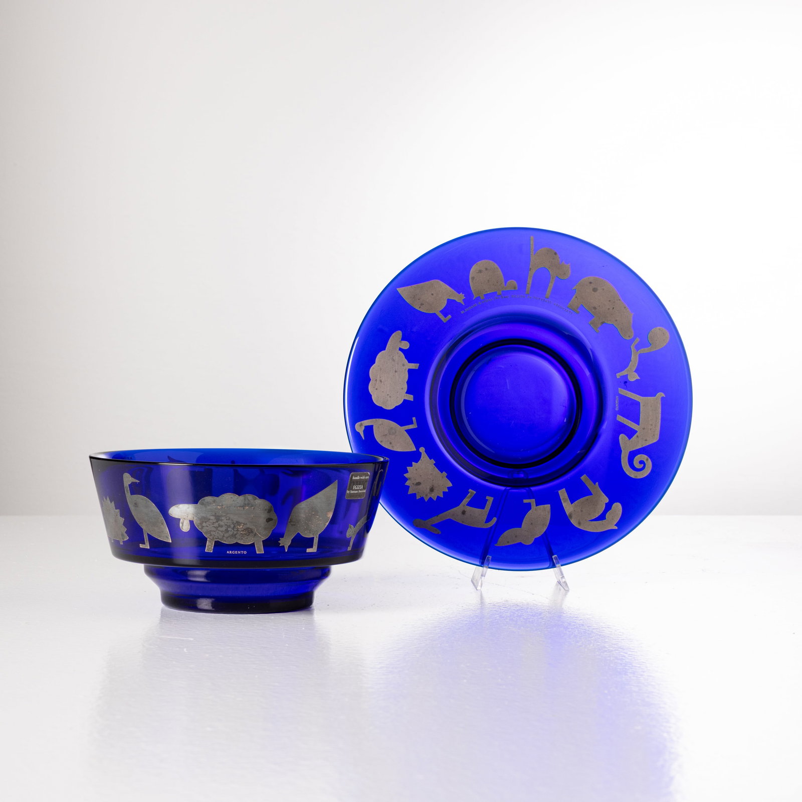 ELISABETH VIDAL & MARCO SUSANI: Ciotola e piatto. Vetro, argento. Produzione Sottsass & Associati, anni '80. Entrambi recano la scritta 'M. Susani ; E. Vidal for hwc Egizia by Sottsass Associati'. piatto cm 3,5x23,5; ciotola cm