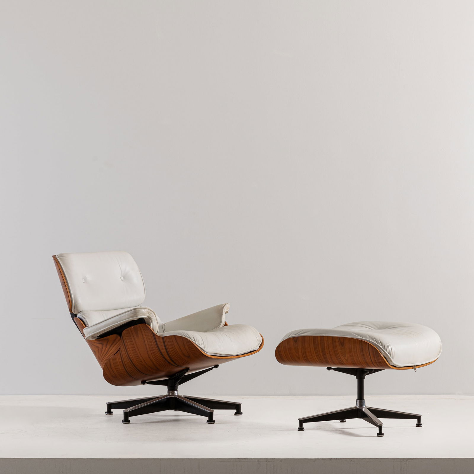 CHARLES & RAY EAMES (DISEGNO DI): Poltrona lounge chair con poggiapiedi. Alluminio pressofuso, legno esotico, pelle imbottita. Italia anni '90. cm 78x83x85; cm 43x66x54 AN ITALIAN LONGUE CHAIR WITH OTTOMAN Buone condizioni
