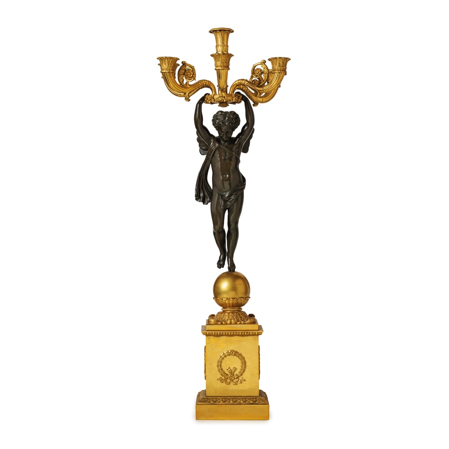 COPPIA DI FLAMBEAUX IN BRONZO PATINATO E DORATO, XIX: SECOLO in stile Impero, a cinque fiamme su cornucopia e una centrale, tutte sorrette da putto alato poggiante su sfera e plinto squadrato; difetti, minori graffi, poche bruniture, alcune bobeches