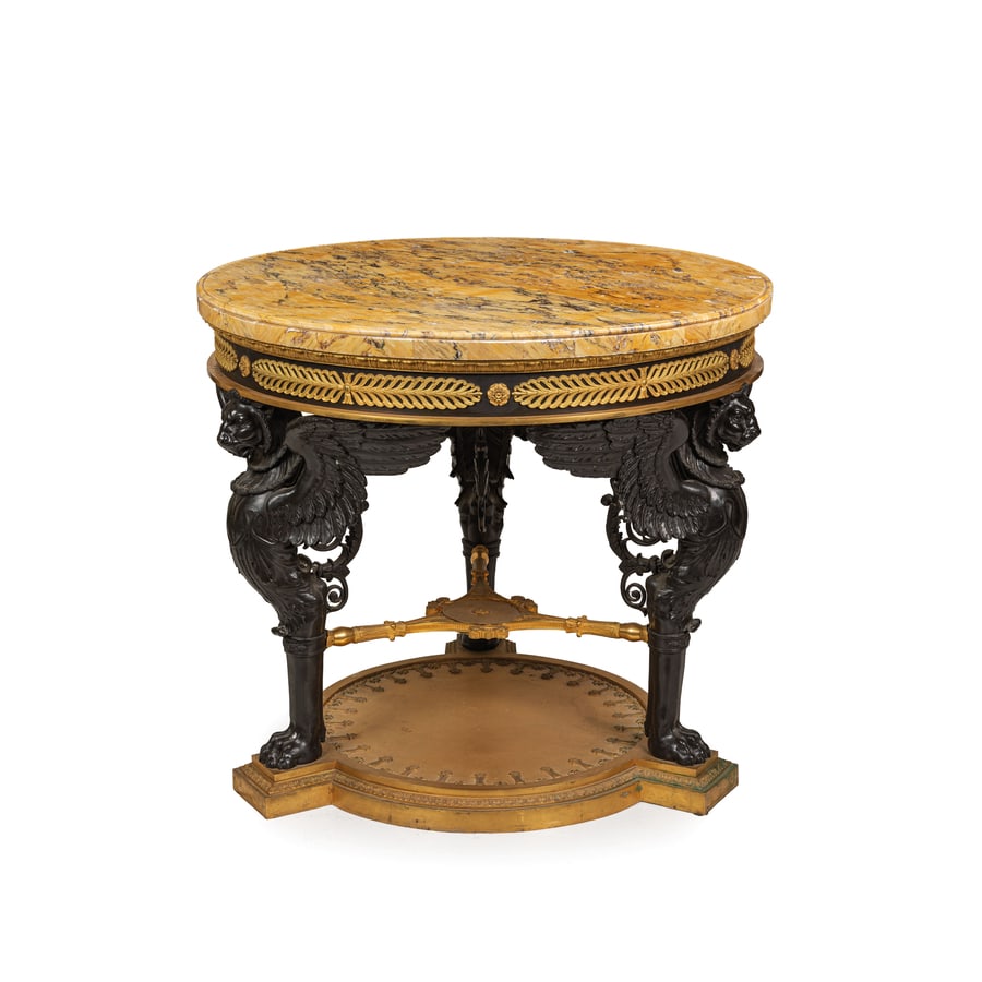 GUERIDON IN BRONZO PATINATO E DORATO, XX SECOLO: in stile Impero, tre montati come leoni monopodi ai lati riuniti da crociera, piano in marmo giallo antico su fascia a tamburo ornata da ricchi fregi a palmette continue; difetti minori, pochi