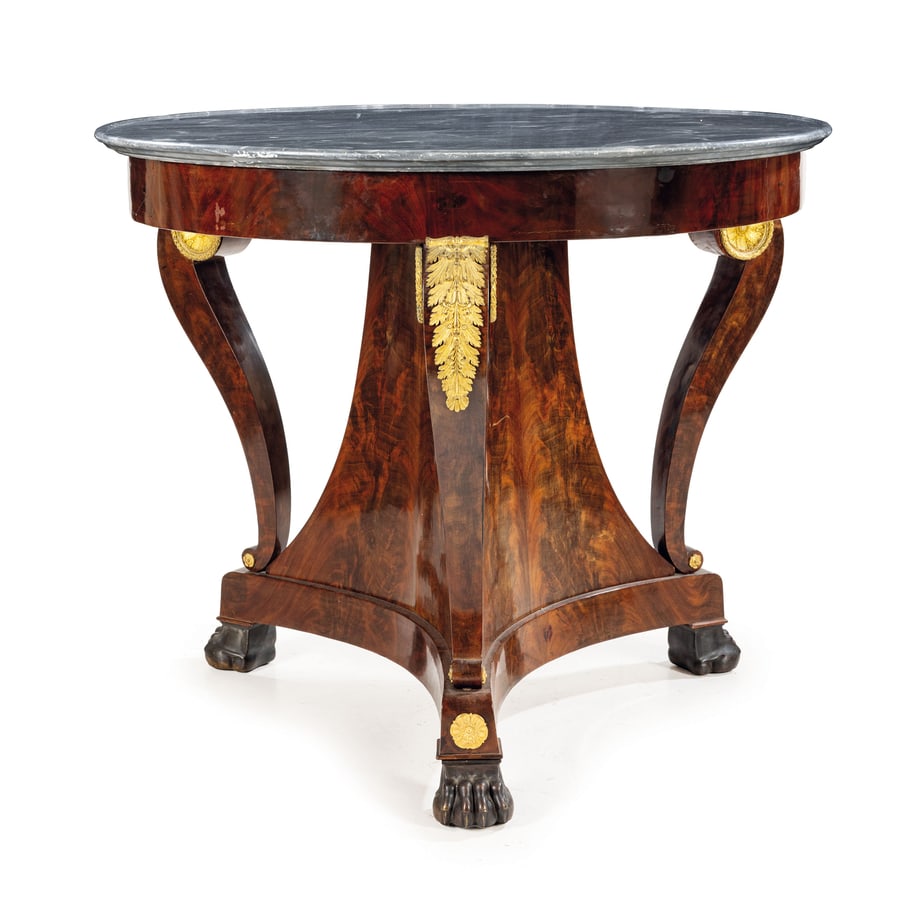 TAVOLO DA CENTRO IMPIALLACCIATO IN PIUMA DI MOGANO: FRANCIA, PRIMA METÀ DEL XIX SECOLO piano a vassoio in marmo grigi venato su fascia circolare a tamburo, tre supporti a doppia voluta con ricche montature in legno dorato e piedi ferini in bronzo