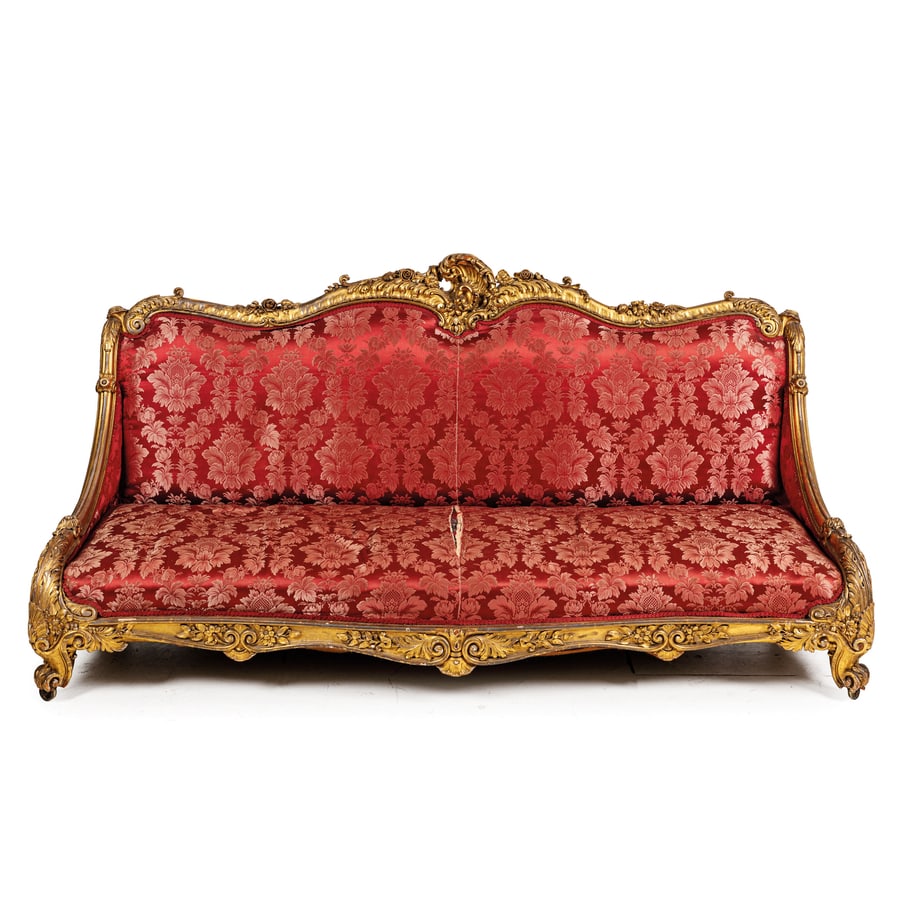 DIVANO IN LEGNO INTAGLIATO E DORATO, XIX SECOLO: ricco intaglio floreale a rilievo, piedi a ricciolo su rotelle, rivestito in tessuto damascato; difetti, mancanze e ritocchi nella doratura, restauri, il tessuto con rotture e lacerazioni, minori manc