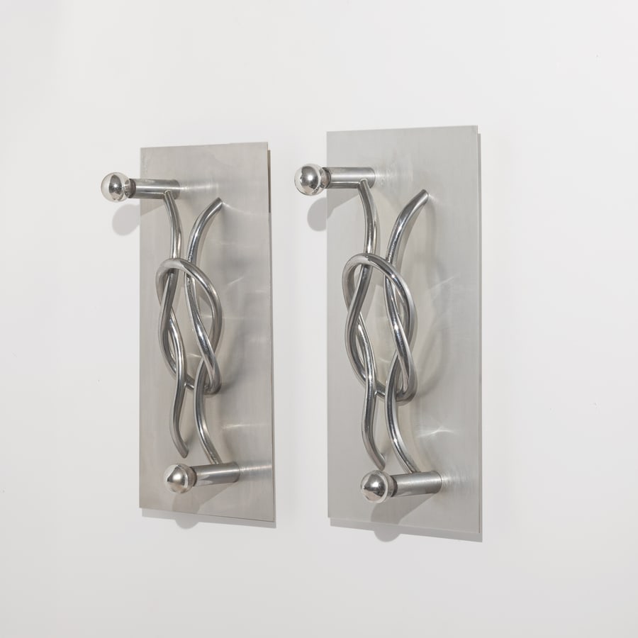 GIACOMO BENEVELLI: Coppia di lampade da parete mod. Nodo. Metallo cromato, metallo satinato. Produzione Gaetano Missaglia anni '70. cm 55x30x18 A PAIR OF WALL LIGHTS BY G. BENEVELLI Buone condizioni generali. Righe,