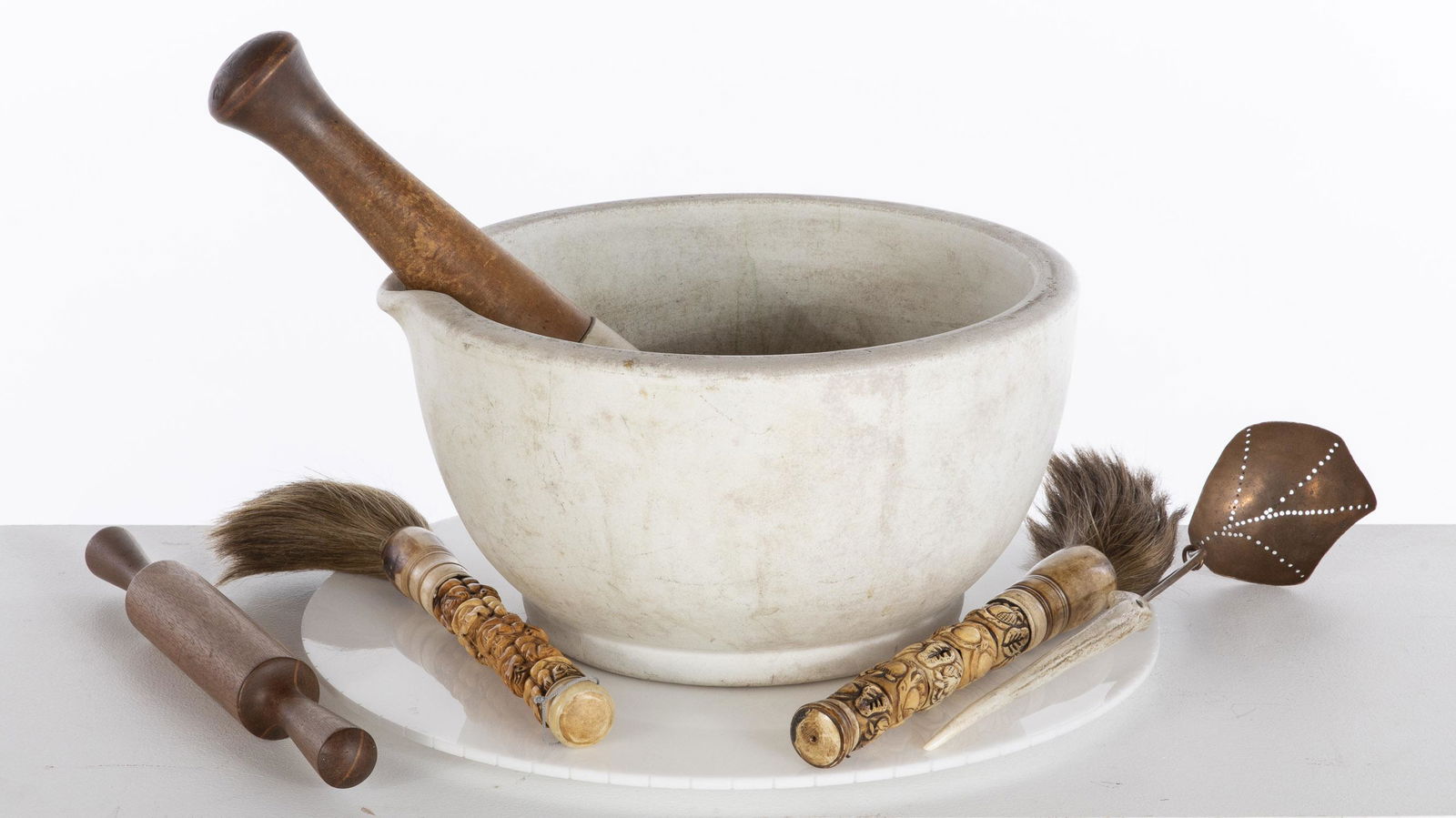 Large Mortar and Pestle and 4 Utensils: Large Mortar and Pestle and 4 Utensils, comprising a large mortar, a pestle with wooden handle, wooden rolling pin, two carved bone paintbrushes, and pierced copper spoon with antler handle. MEASURMEN