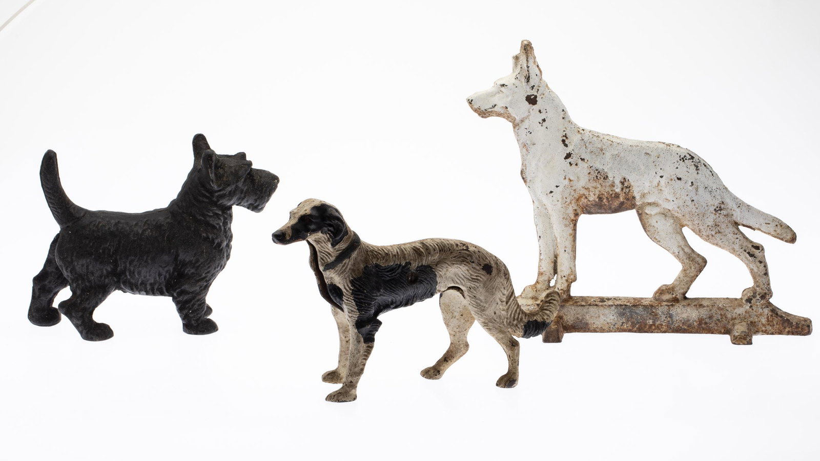 3 Painted Cast Iron Dogs: Property from a Private Collection Ponte Vedra, FL Description: 3 Painted Cast Iron Dogs, comprising a painted cast iron Scottie dog, a black and white painted hound dog, and a white painted Germa