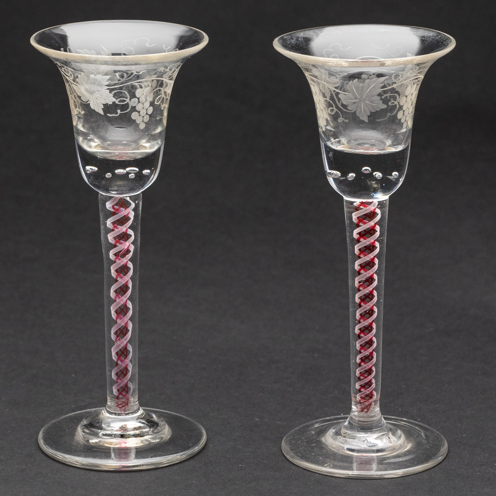 Pair English Glasses w/ Red Air-Twist Stems, 18th C: Property from a Private Collection, Charleston, SC Description: Pair of English Wine Glasses with Red Air-Twist Stems, 18th C, with red air-twist stems and etched with grapes. Measuremen