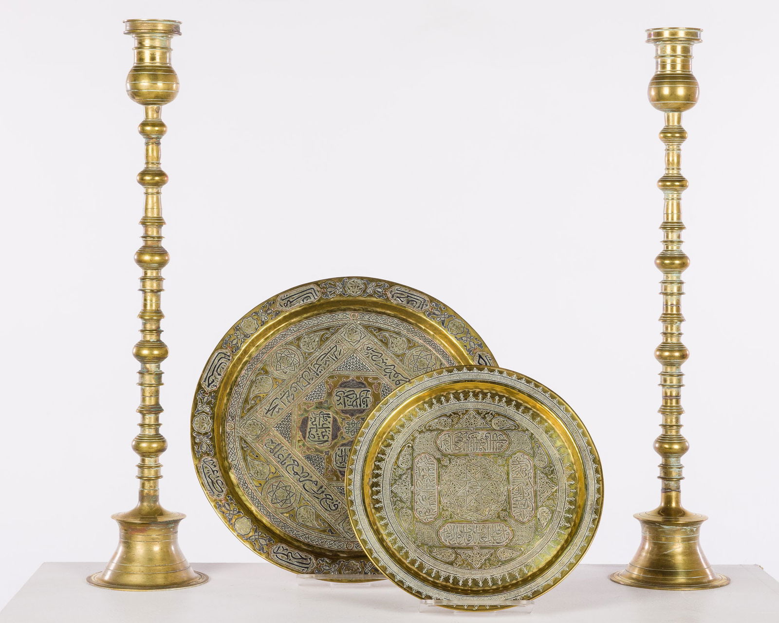Pair of Large Brass Candleholders and 2 Syrian Brass Trays: Property of a Diplomatic World-Traveling Family Description: Pair of Large Brass Candleholders and 2 Syrian Brass Trays, comprising a pair of large brass candlesticks, a 13 in. platter and a 17 1/