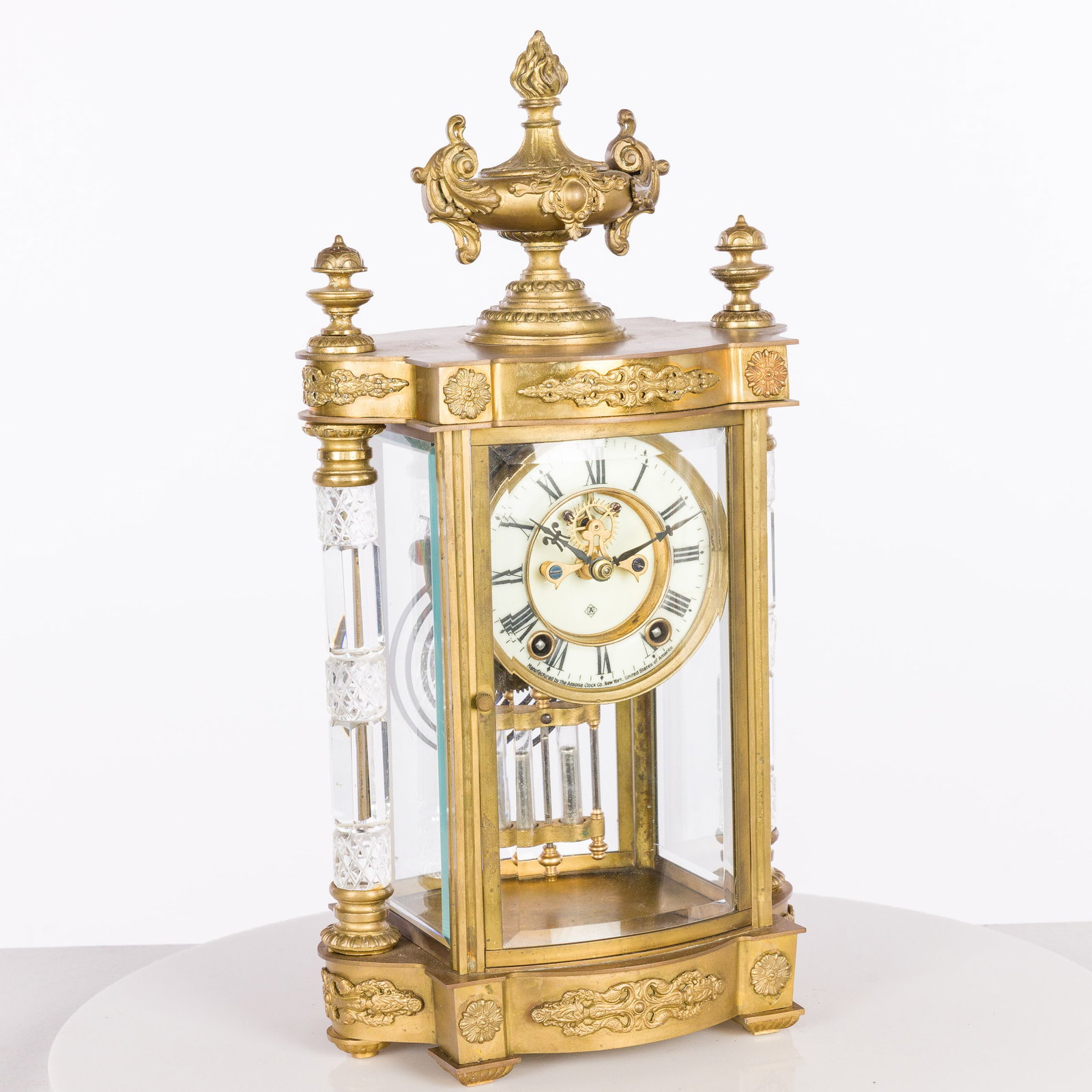 Ansonia Jupiter Clock: Property from a Naples, FL Estate Description: Ansonia Jupiter Clock, polished brass and gold ornaments, cut glass columns, convex doors with 8 day hour and half hour gong strike, visible escapeme