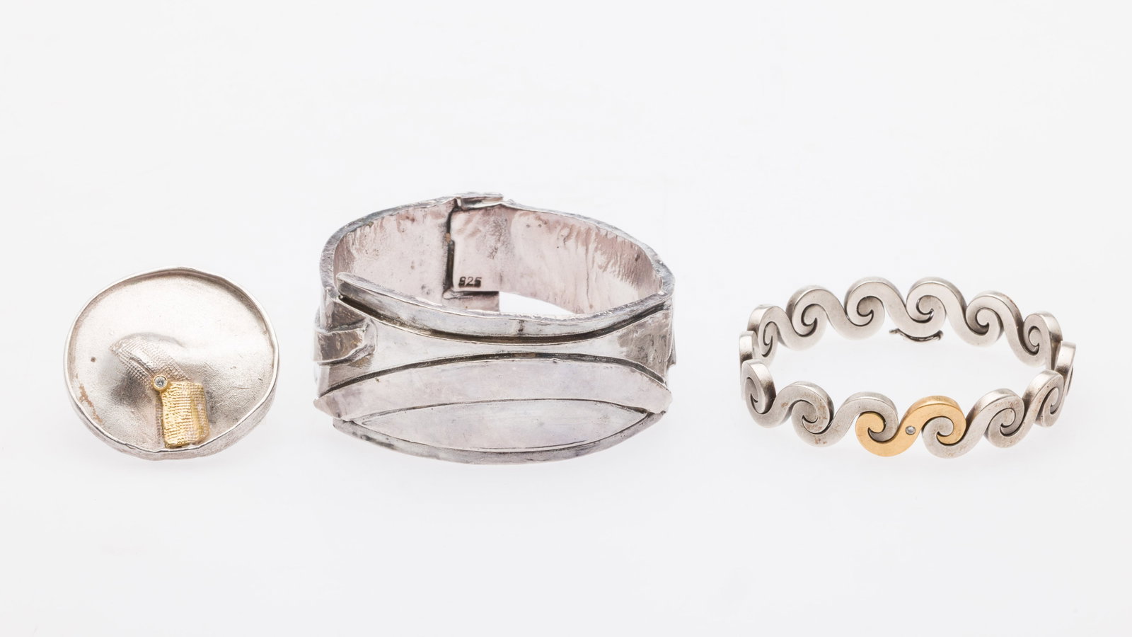 Two Sterling Bracelets and a Pin/Pendant: Description: Two Sterling Bracelets and a Pin/Pendant, comprising a sterling silver textured wide bangle bracelet (marked 925 on inside); a sterling silver wave link bracelet with one 22k link an