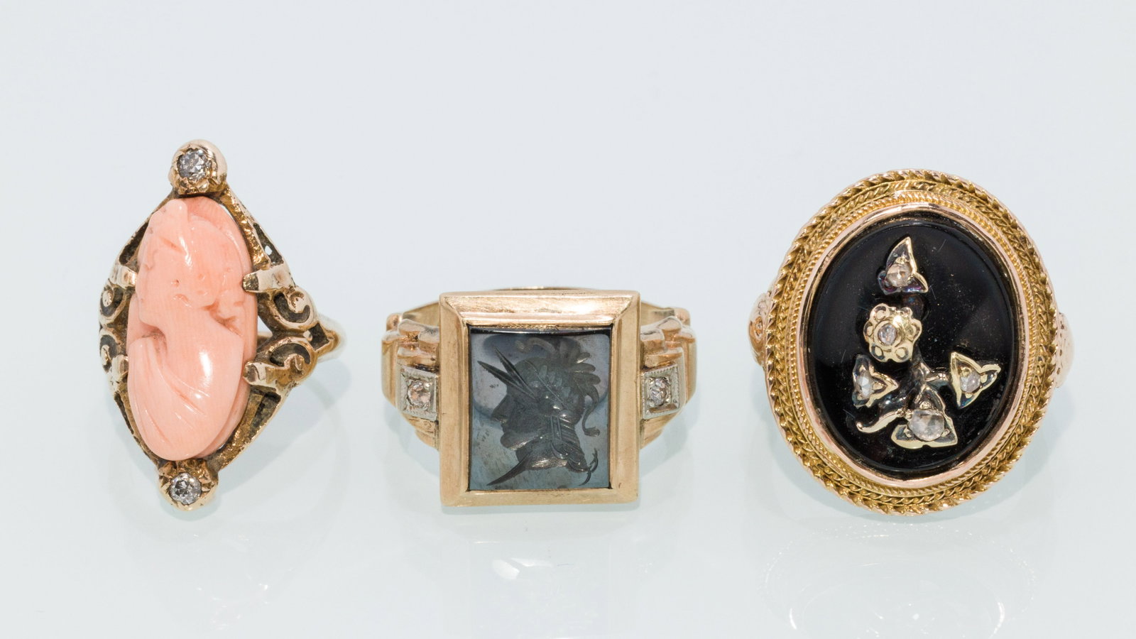 Trio of Vintage Rings with Hematite, Coral, and Onyx: Description: Trio of Vintage Rings with Hematite, Coral, and Onyx, comprising a 10K yellow gold ring with Hematite cameo flanked by two small diamonds, size 7.25 (marked '10K'); a 10K yellow gold