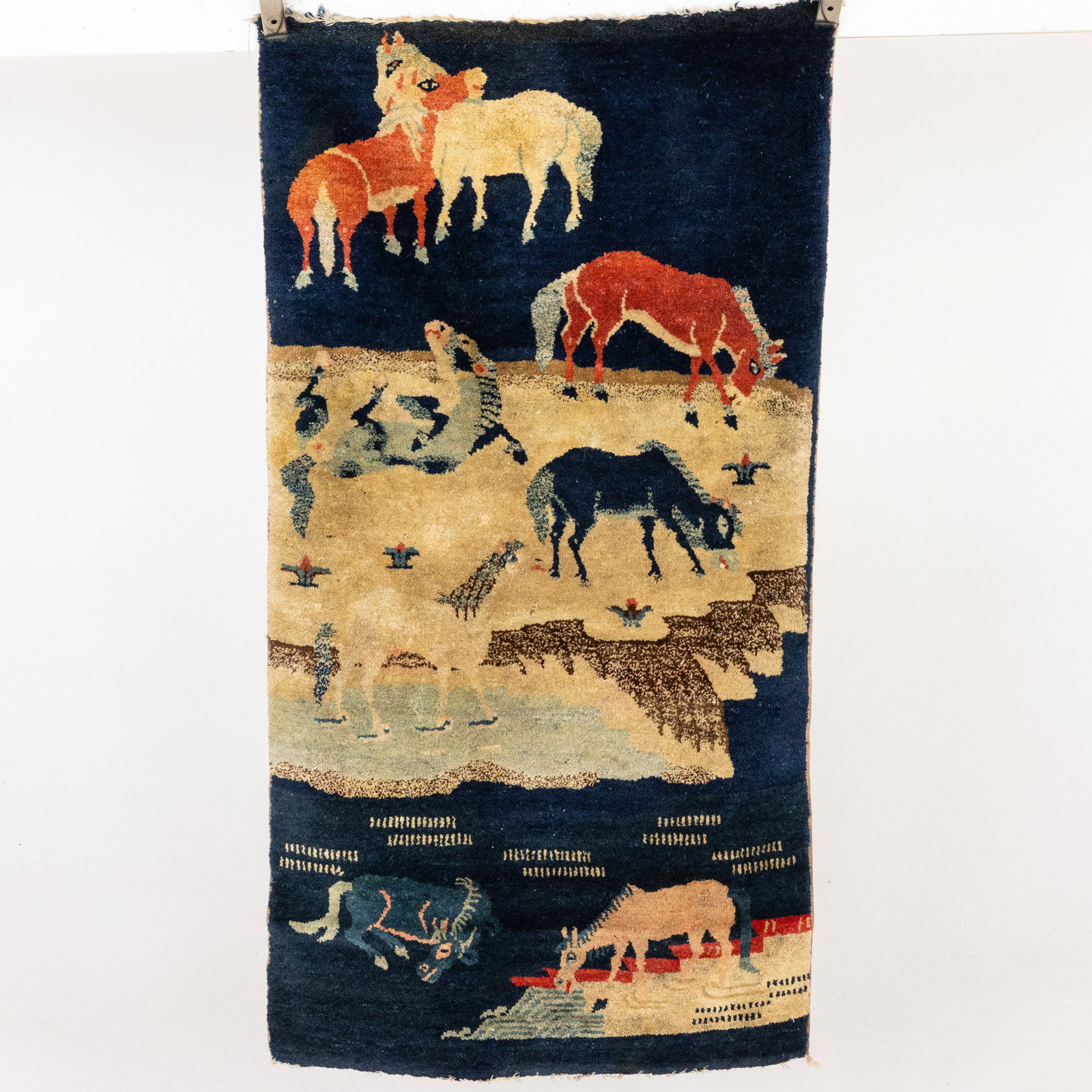 Small Chinese Rug with Horses: Property from a St. Simons Island, GA Estate Description: Small Chinese Rug with Horses, in tones of cream, red, and beige on a dark blue ground. Measurements: Length: 48 1/2 in