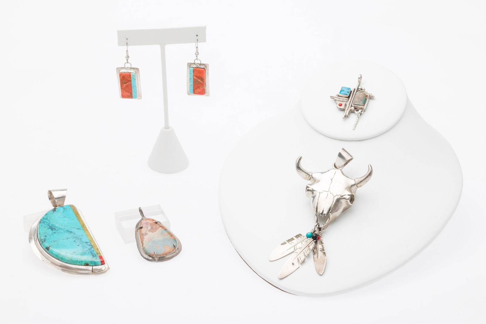 4 Native American Pendants & Pair of Earrings: Description: 4 Native American Pendants, Including Ray Tracey & Pair of Earrings, comprising a 4 3/8 in. Ray Tracey skull shaped silver pendant with blue, black, and orange beads on feather drops