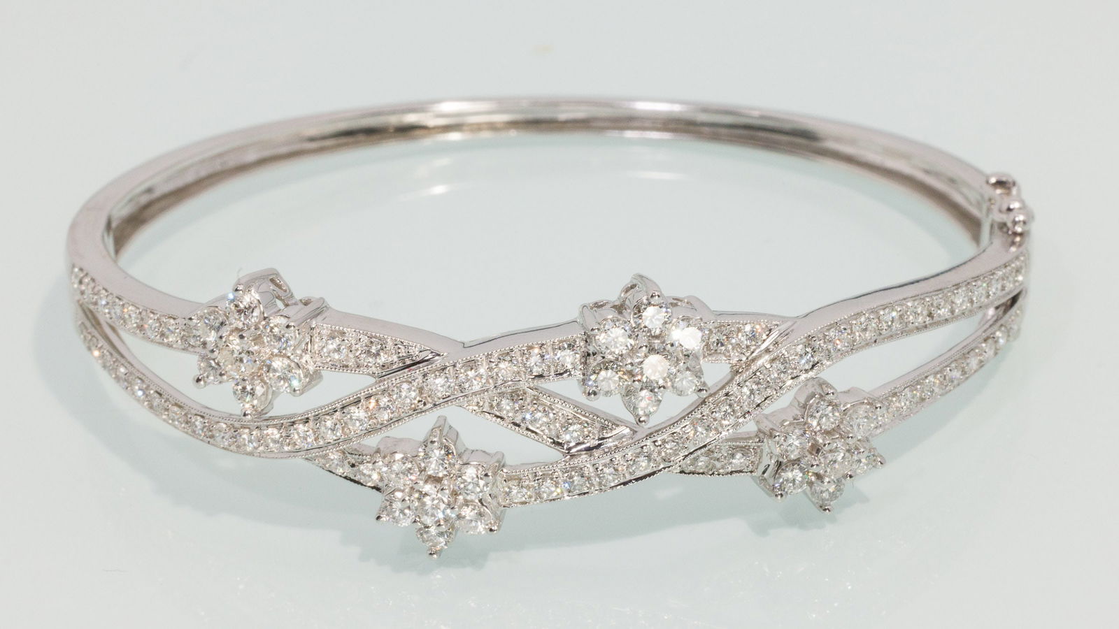 14K Gold and Diamond Flower Bangle: Description: 14K Gold and Diamond Flower Bangle, 14K white gold bangle bracelet featuring various round cut diamonds set in a twisting flower design, (approx. 3 cts, F-G, VS), with hinge and locking