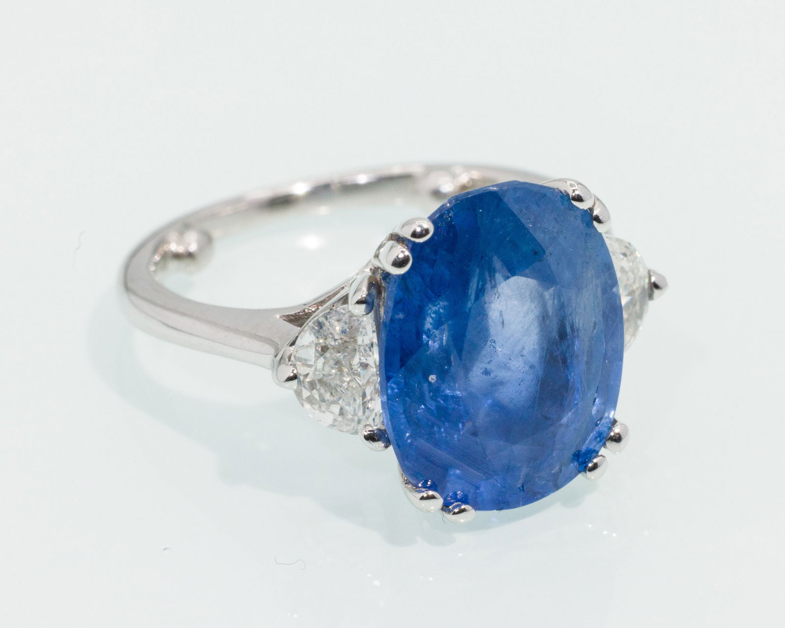 Burmese Sapphire, Diamond and 18K Ring: Description: Burmese Sapphire, Diamond and 18K Ring, 18K white gold ring featuring a prong set oval mixed cut blue sapphire (Burma, no heat, 6.88 cts) flanked by two halfmoon cut diamonds (approx.