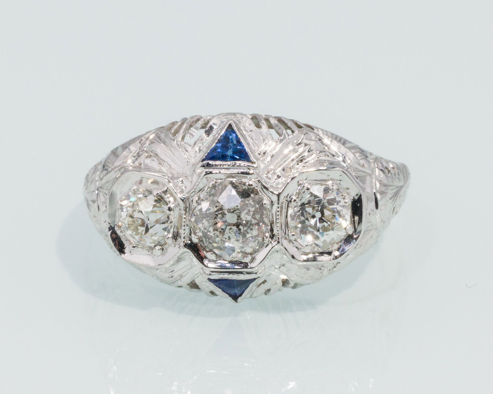 Art Deco 18K, Diamond and Sapphire Ring: Description: Art Deco 18K, Diamond and Sapphire Ring, 18K white gold ring featuring three old mine cut diamonds (approx. 1 cts overall), the center stone flanked by two triangular cut sapphires, the