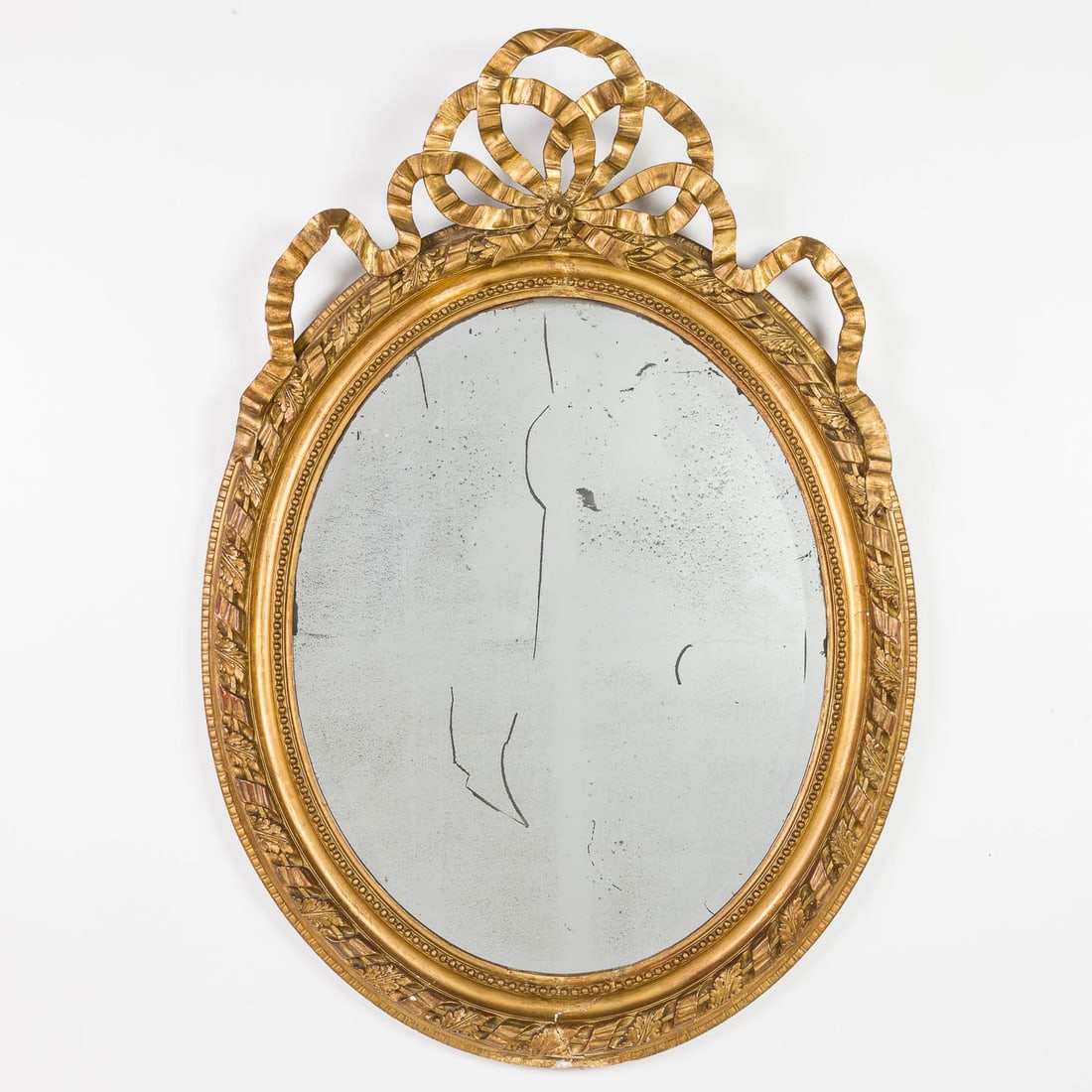 French Louis XVI Style Giltwood Oval Mirror, 19th C: Property from a Private Collection, New York City Description: French Louis XVI Style Giltwood Oval Mirror with Bow Crest, the oval mirrorplate within a carved surround surmounted by a bow.