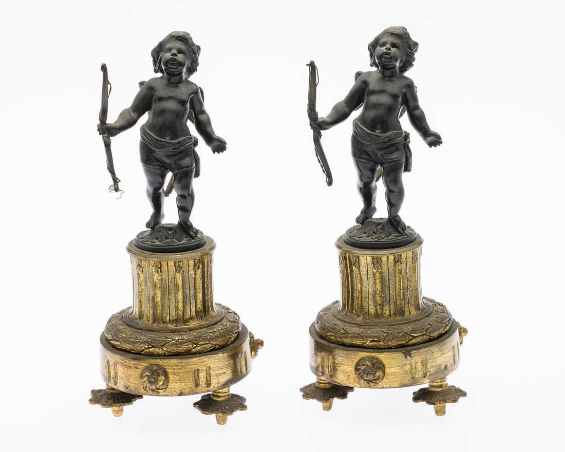 Pair of French Gilt Bronze Cherub Garniture: Description: Pair of French Gilt Bronze Cherub Garniture, each with ebonized bronze cherub figures on columnar gilt bronze base with tripod feet, likely previously candlesticks. Measurements: Height: