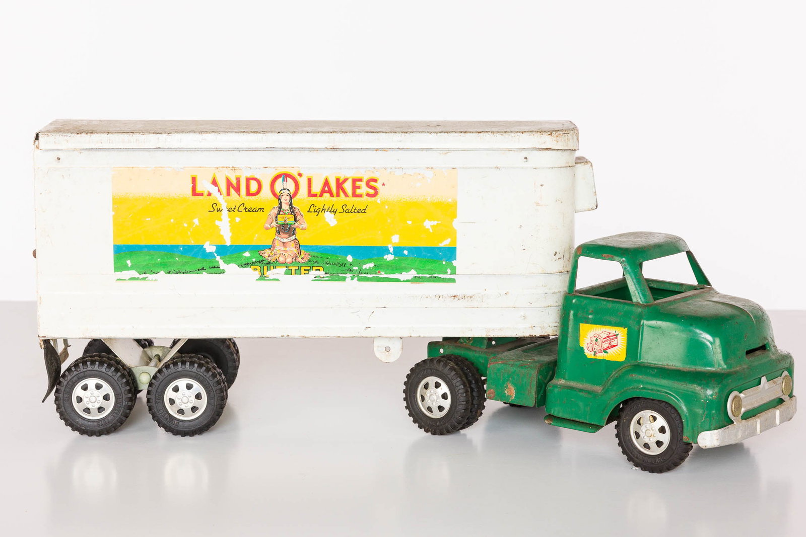 Ohio Art Dunwell Buckeye Land-O-Lake Truck, c 1950s: Description: Ohio Art Dunwell Buckeye Land-O-Lake Semi Truck, c. 1950s, with green cab and removable white Land-O-Lakes branded trailer, with 'Dunwell Certified Toy' label on bottom of cab.