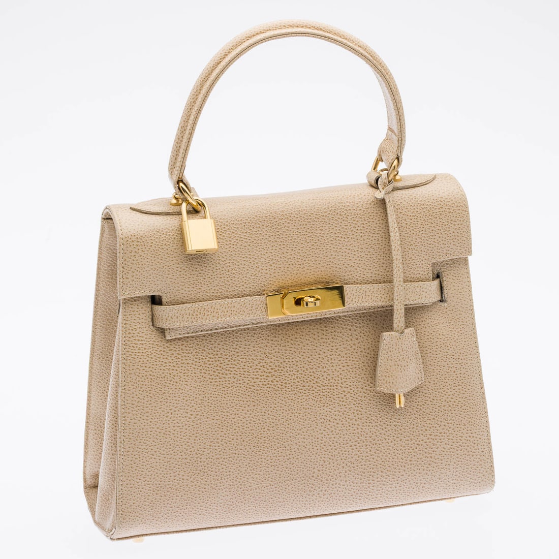Kelly Style Lionheart Buff Leather Handbag: Description: Kelly Style Lionheart Buff Leather Handbag, with a structured trapezoidal shape, a single top handle, front toggle latch closure, internal zipper pocket, thin removable strap, and brand