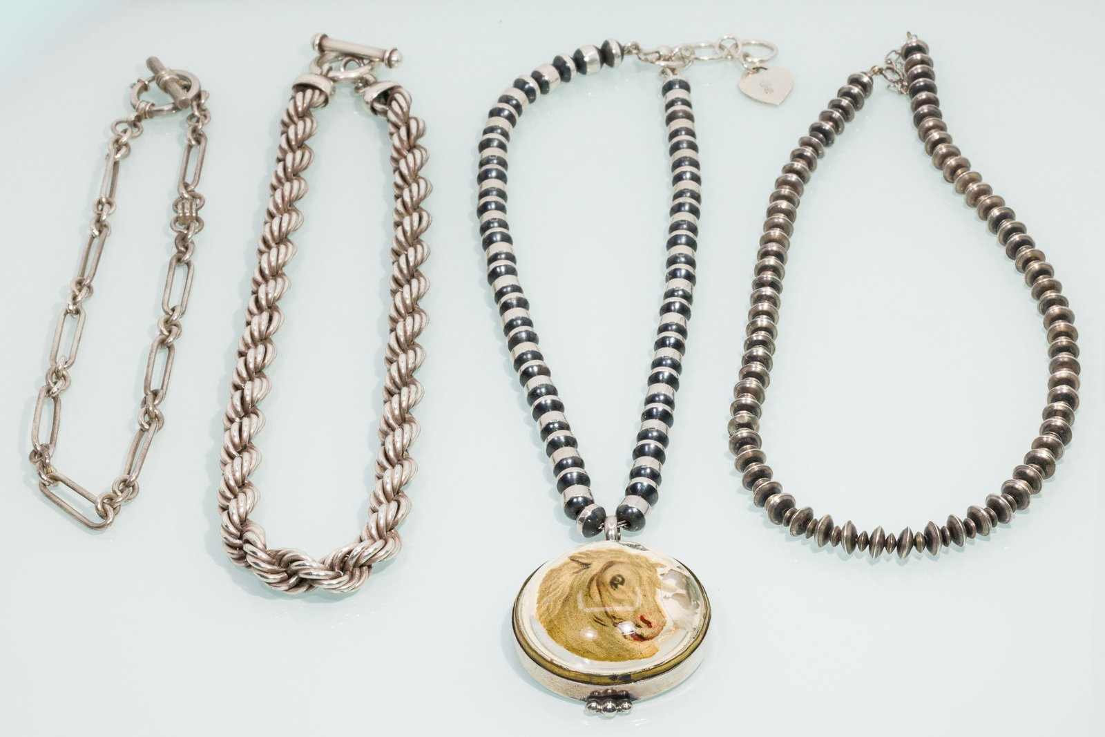 Four Silver Necklaces, One with Glass Horse Pendant: Property from a Savannah, GA Estate Description: Four Silver Necklaces, One with Glass Horse Pendant, comprising a 15 in. wide link sterling silver chain with hook and loop clasp (marked '925', 1.