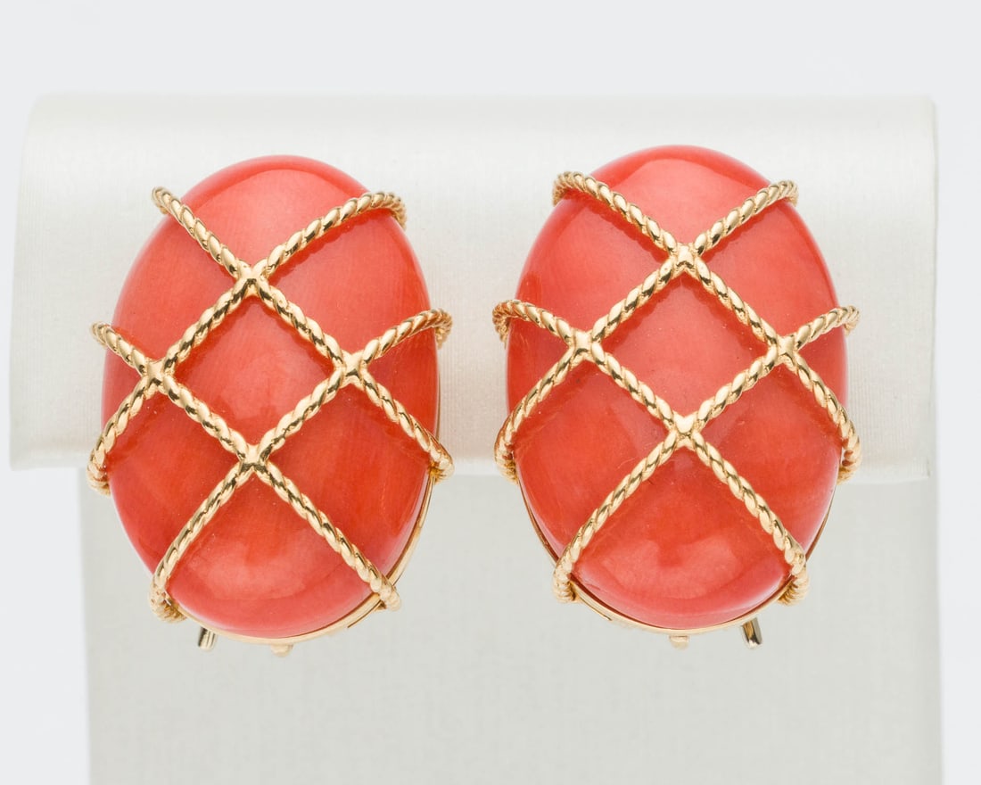 Coral and 18K Earrings: Description: Coral and 18K Earrings, each featuring an oval coral cabochon with yellow gold cage design overtop, with clip and movable post backs, marked '750'. 15.15 grams overall. Measurements: