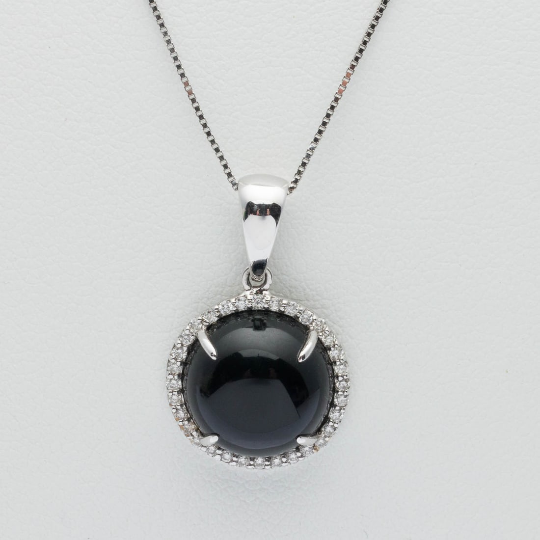 14K White Gold, Black Onyx and Diamond Pendant: Description: 14K White Gold, Black Onyx and Diamond Pendant, featuring an approx. 11 mm round onyx cabochon with diamond halo (approx. 0.15 cts) set in 14K white gold, marked 'DC750, 18K' on pendant
