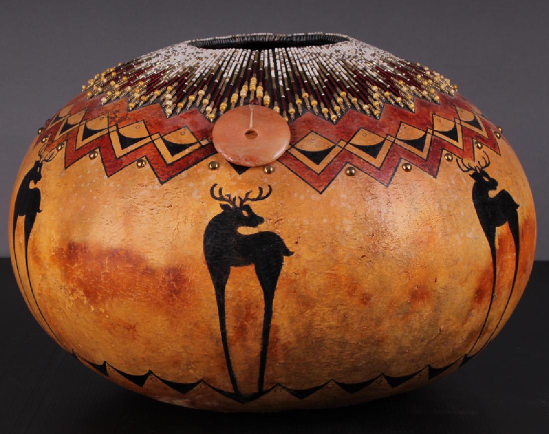 Southwestern Art: Artist Unidentified (20 th Century): Painted gourd with elaborate beadwork, metal studs and hanging stone, stamped DES, 10â€ tall, 15â€ diameter.
