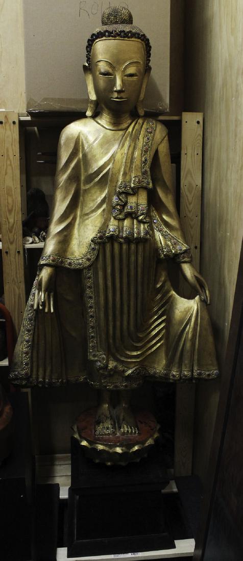 Asian Decorative Art: Thai Statue: STANDING BUDDHA, carved wood with gold finish and embedded colored glass, 63 ½” tall, with painted wood stand overall approximately 75 ½ x 30 x 16 ¼”. From the private collection of Academy Awa