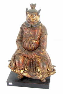 Asian Statue: SEATED CHINESE DEITY, Qind dynasty, cast metal sculpture with traces of gilt and red lacquer remnants, 15 ½" tall, 10" wide, 5 ½" deep, seated on a wood base, overall wear and surface losses from ag