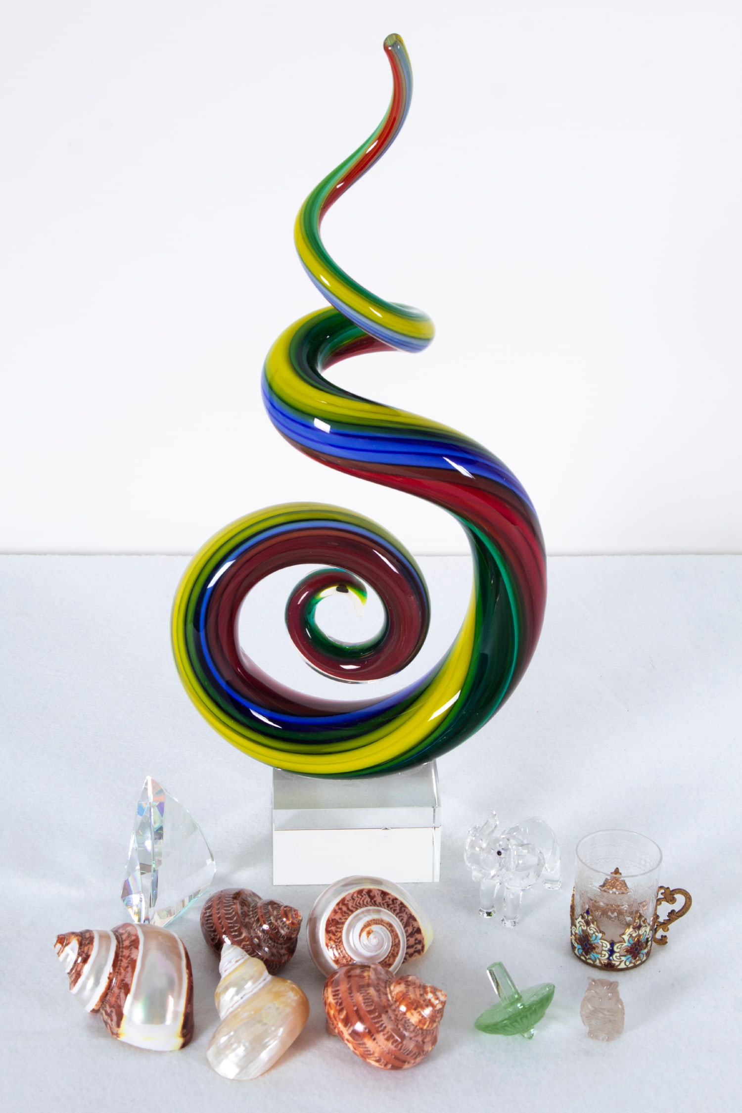 Decorative Objects: Glass (eleven): A 2 ¾” anodized crystal paperweight; A 14 ½” tall clear and color glass swirl, including base; A 2 ½ x 1 ½ x 2 ½” cut- crystal elephant figurine; A