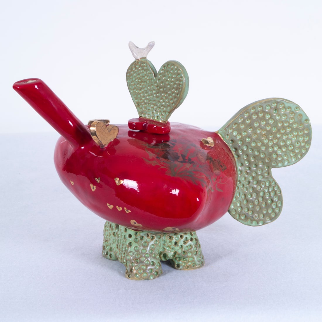 Meg Johnson (20 th Century) California: Red heart with butterflies, painted glazed and gilded ceramic teapot, signed underneath, 8 ¾” tall, 12 ½” wide. Acquired from/ Provenance: Art Options February 1992.
