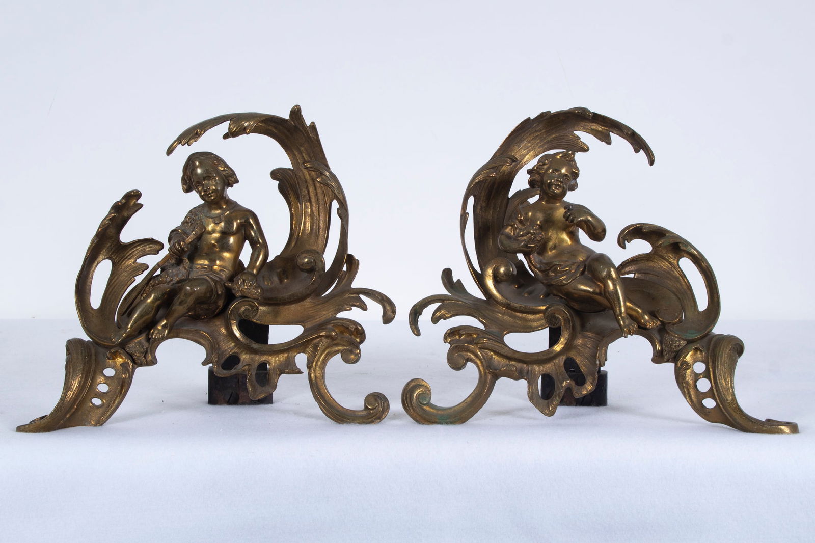 Bronze Cupid Andirons (two): CUPIDS, a pair of cast bronze andirons with iron footings, both with illegible stamps and numbering, each approximately 10 x 12 ½ x 5 ½”. (2)