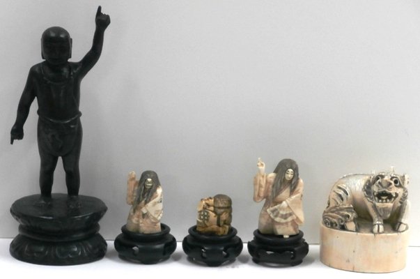 Decorative Items: Netsuke & Japanese Carvings & Pri: Elaborately carved seal, 3 ¼” tall; Together with NETSUKE, three carved figurines, 1 ¼” to 2 ¼” tall, each with wood stand, one small figure possibly lacking part of stick, some minor discolo