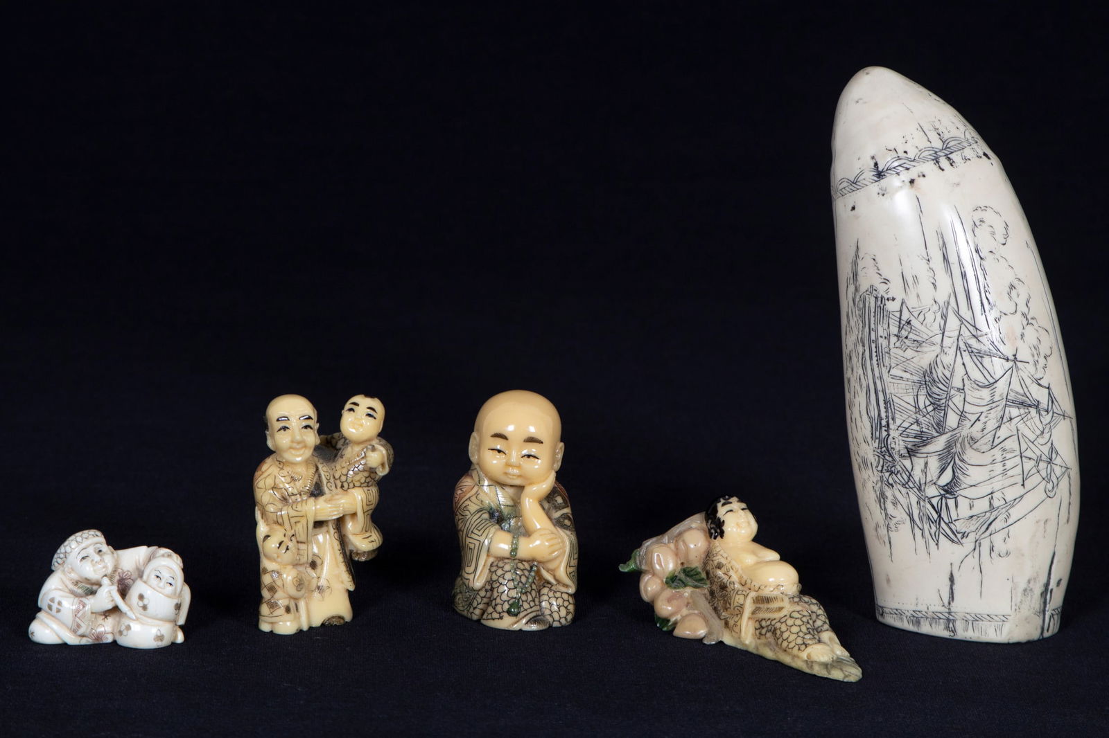 Netsuke (four) & Scrimshaw (one): Four carved figures: Seated Boy; Man with Children; Man with Wrapped Baby; Reclining Buddha, sizes from 2 ¼” to 1” tall, two signed underneath; Together with a carved scrimshaw horn
