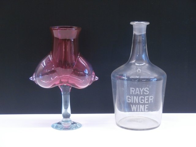 Ray Jacobs (b. 1928) & Contemporary Glass (two): Ray Jacobs, RAY’S GINGER WINE, etched clear glass bottle, 11 ½” tall, 6” diameter; Together with Unidentified Artist, BOOB GLASS, cranberry to clear glass, 10 ¾ x 7 ¼ x 3 ¼”, both in good 