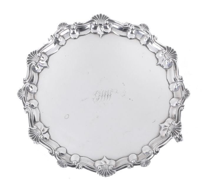 A George III silver shaped circular salver by Rich: A George III silver shaped circular salver by Richard Rugg, London 1779, the raised border with a scroll and shell rim, on three ball-and-claw feet, later engraved with initials 'GNW', 31cm (