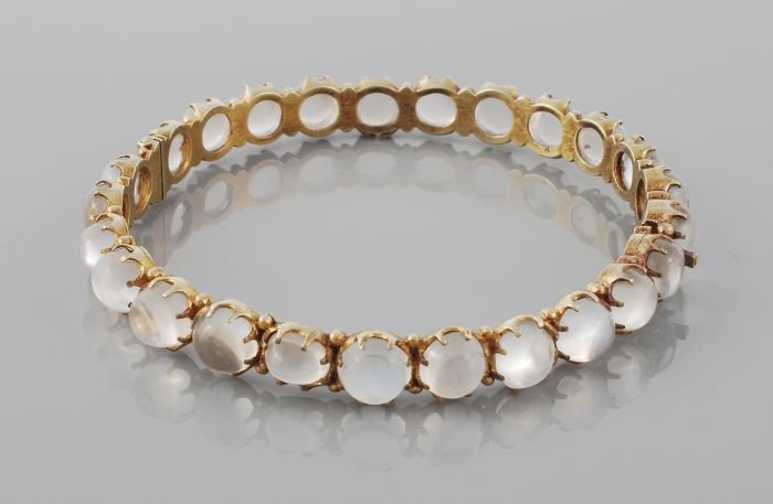 A moonstone bangle, the hinged bangle claw set all: A moonstone bangle, the hinged bangle claw set all around with twenty five circular and oval moonstone cabochons, 5.9cm inner diameter