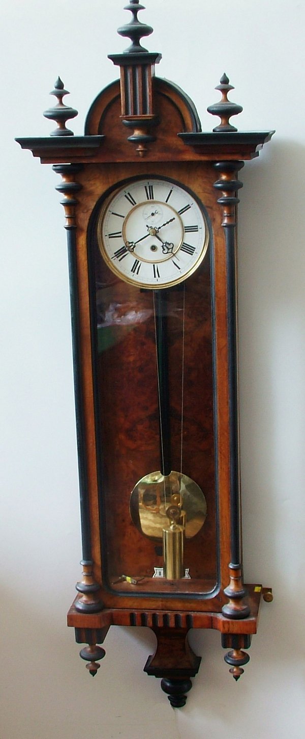 Vienna type regulator wall clock, enamelled metal: Vienna type regulator wall clock, enamelled metal dial with subsidiary seconds, single train weight-driven movement, ebonised pendulum rod, in figured walnut case. Length 134cm. (Weight, key, pendulum