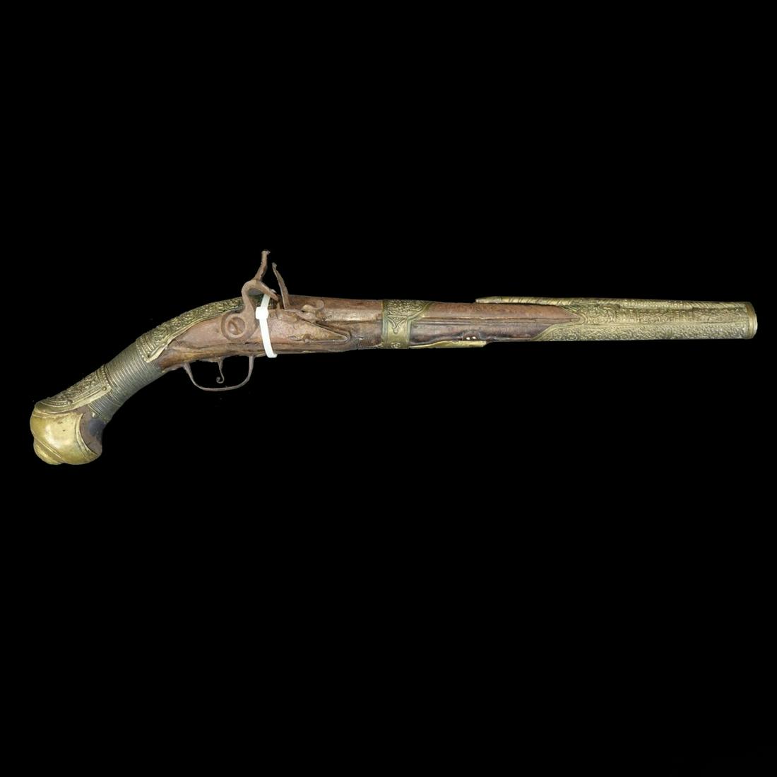 20th C. Turkish Flint Lock Pistol: Early to mid 20th Century Turkish Flint Lock Pistol. Chased brass decorative mounts along the handle and barrel, engraved barrel. Measures 21-1/2" L. Condition: Corrosion to surface, wear otherwise go
