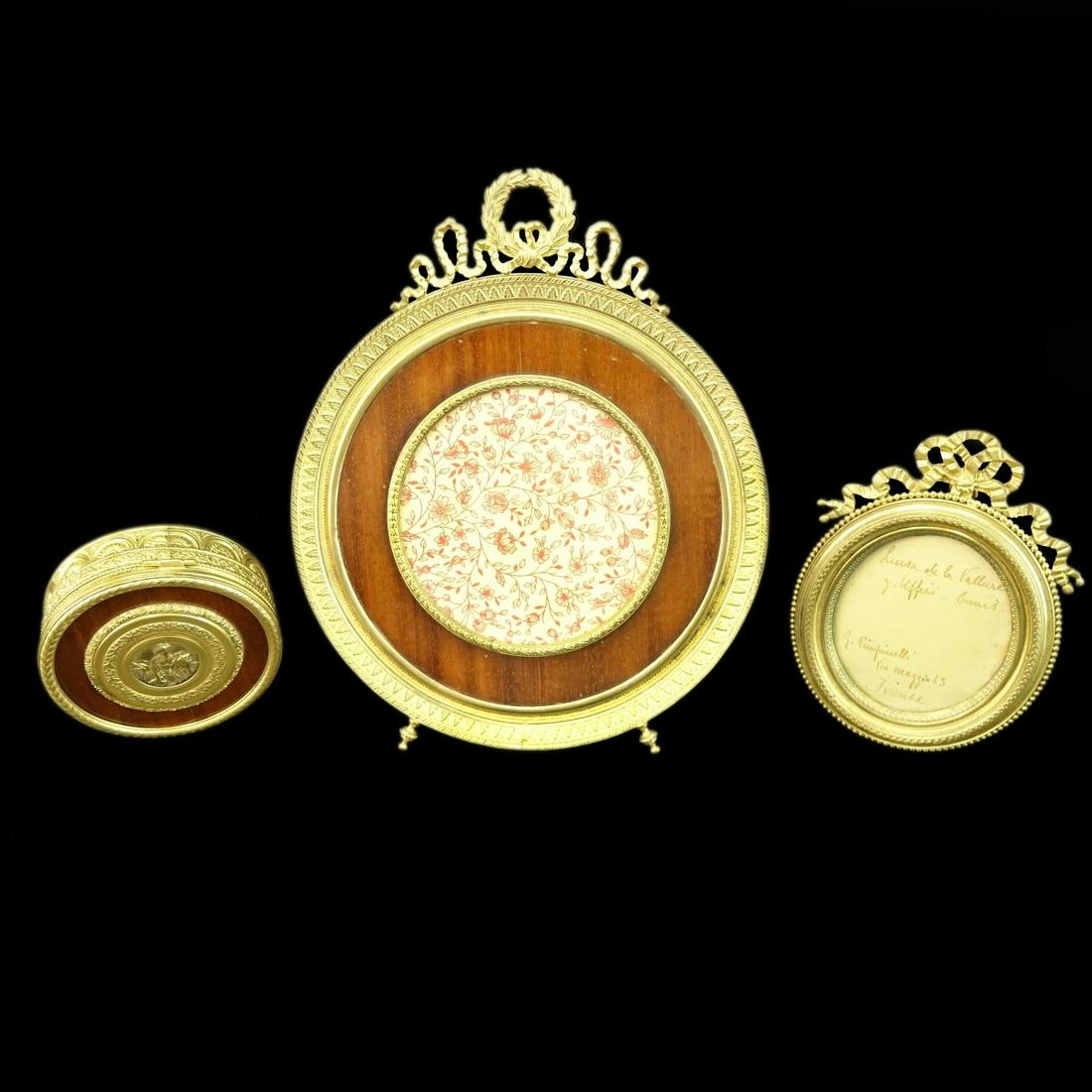 3 Gilt Bronze Mounted Table Top Items: Three (3) Gilt Bronze Mounted Table Top Items. Two picture frames small oval 5-1/4" H, large round 8-7/8" H, and a Round hinged box with a medallion of a woman with horse and bronze accents marked Ger