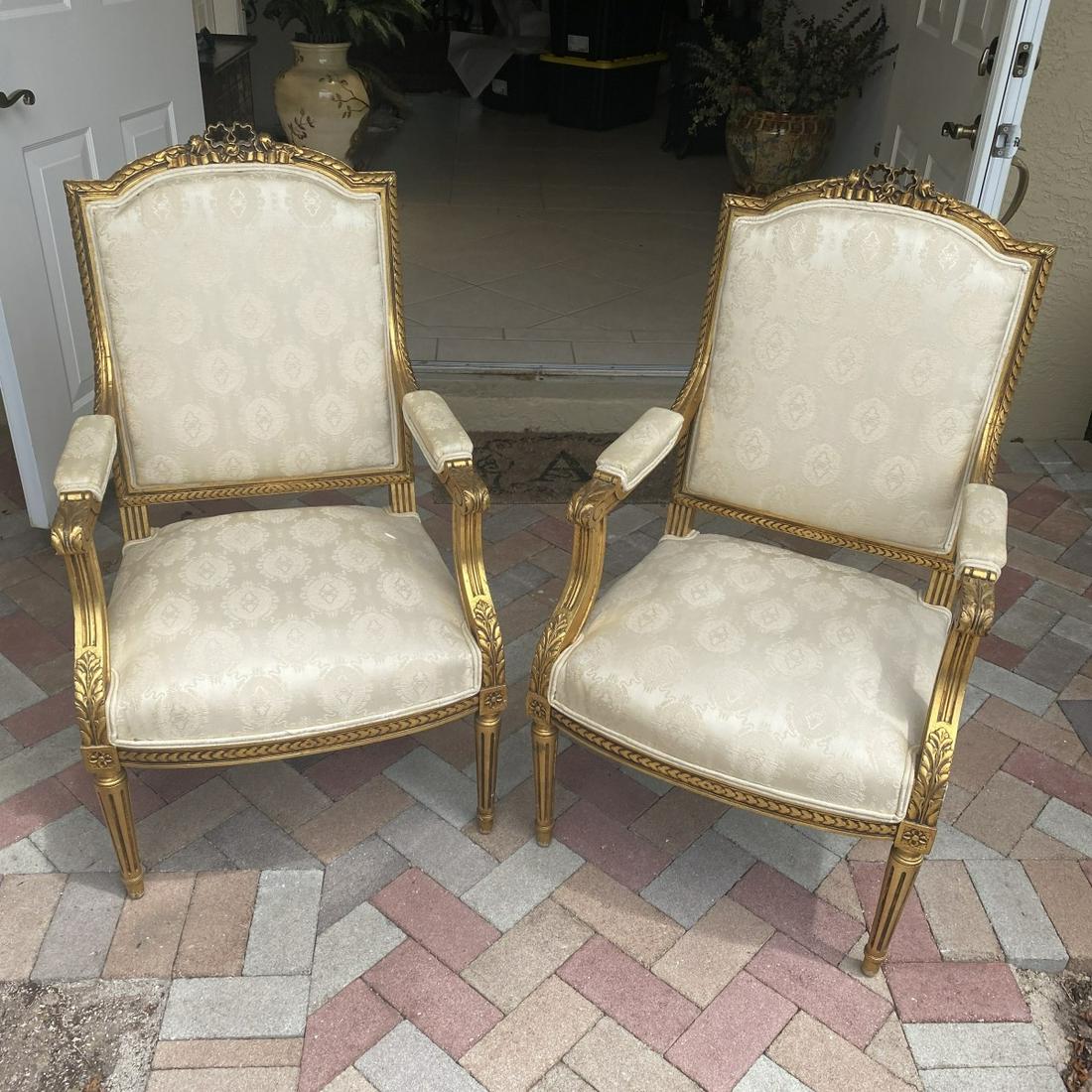 Louis XVI Style Fauteuils: Pair of French Louis XVI Style Gilt Carved Fauteuils. Ribbon finial detail, acanthus leave motif, and stands on cabriole legs. Measures 40-1/2" x 22-3/4" x 24". Condition: Good condition. Estimate: $2