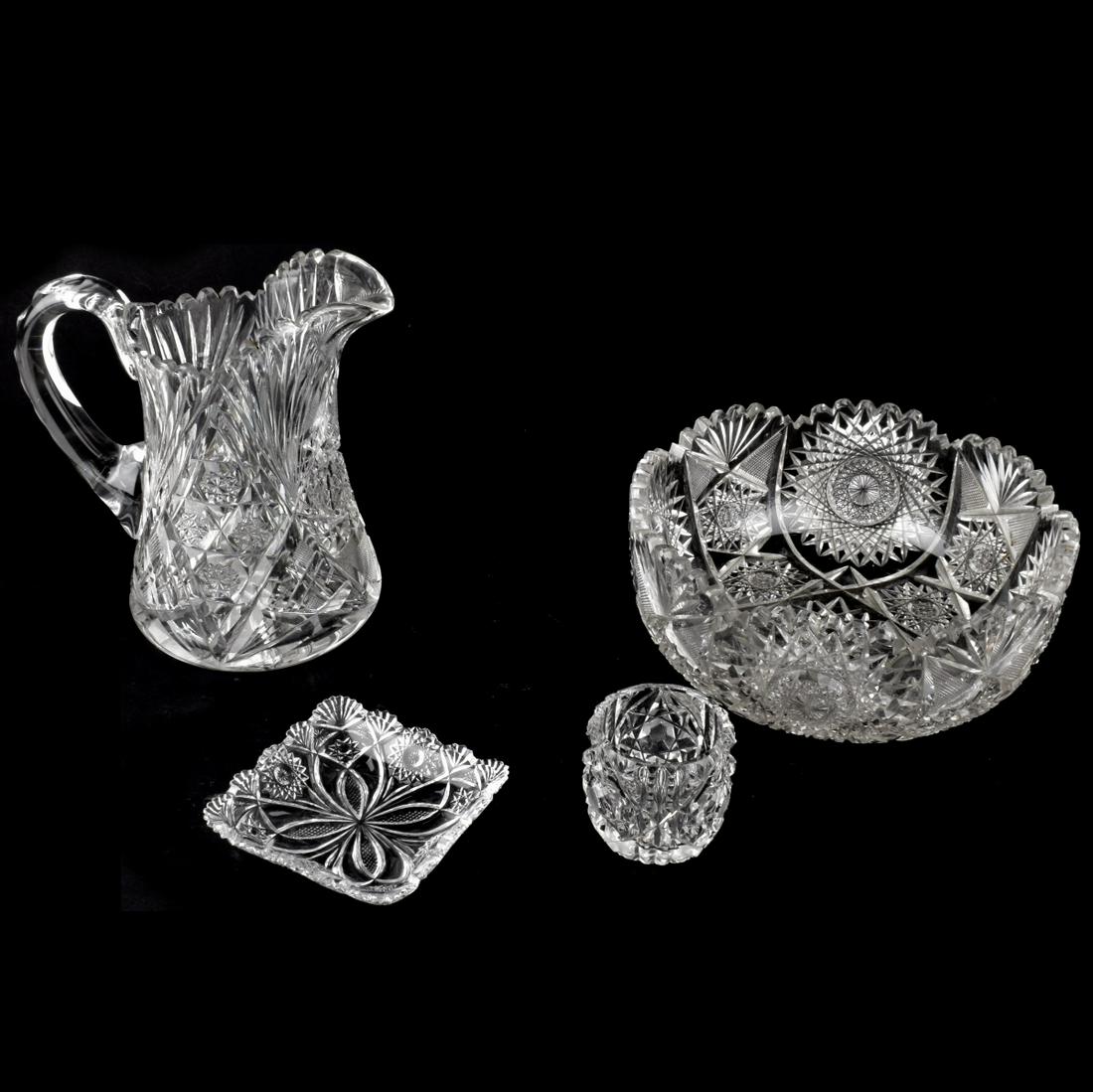 Tableware: Grouping of Four (4) Brilliant Glass Tableware. Includes a pitcher, bowl, cup, and a dish. Pitcher measures 8" x 8" x 5-3/4". Bowl measures 3-3/4" x 9". Condition: Bowl has a small chip to the rim oth