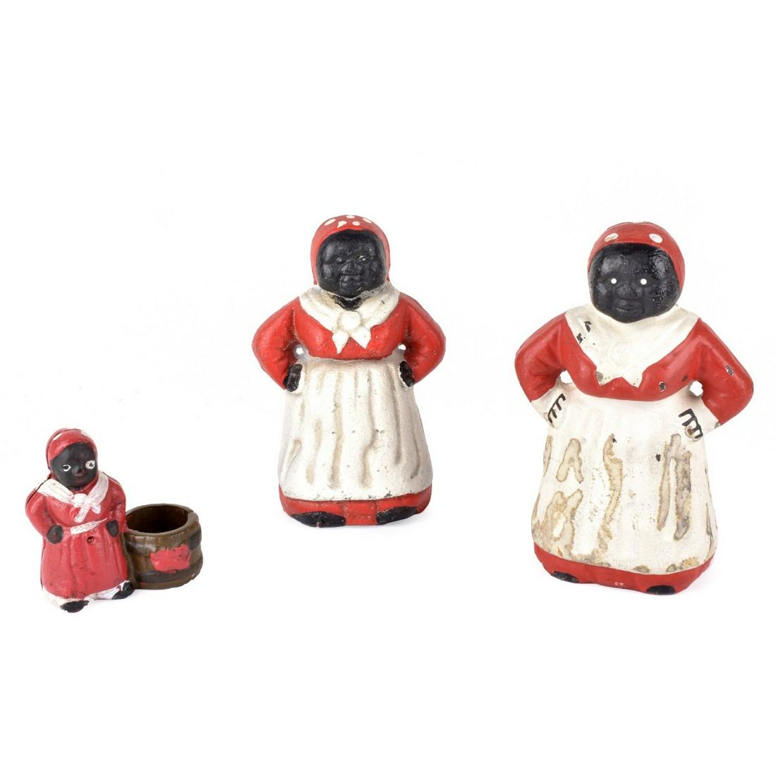 Black Americana Figures: Grouping of Three (3) Early 20th Century Black Americana Cast Iron "Mammy" Figures Attributed to Hubley. Unsigned. Includes: coin bank, door stop, and a candle holder. Coin bank measures 7-1/2" x 4" x