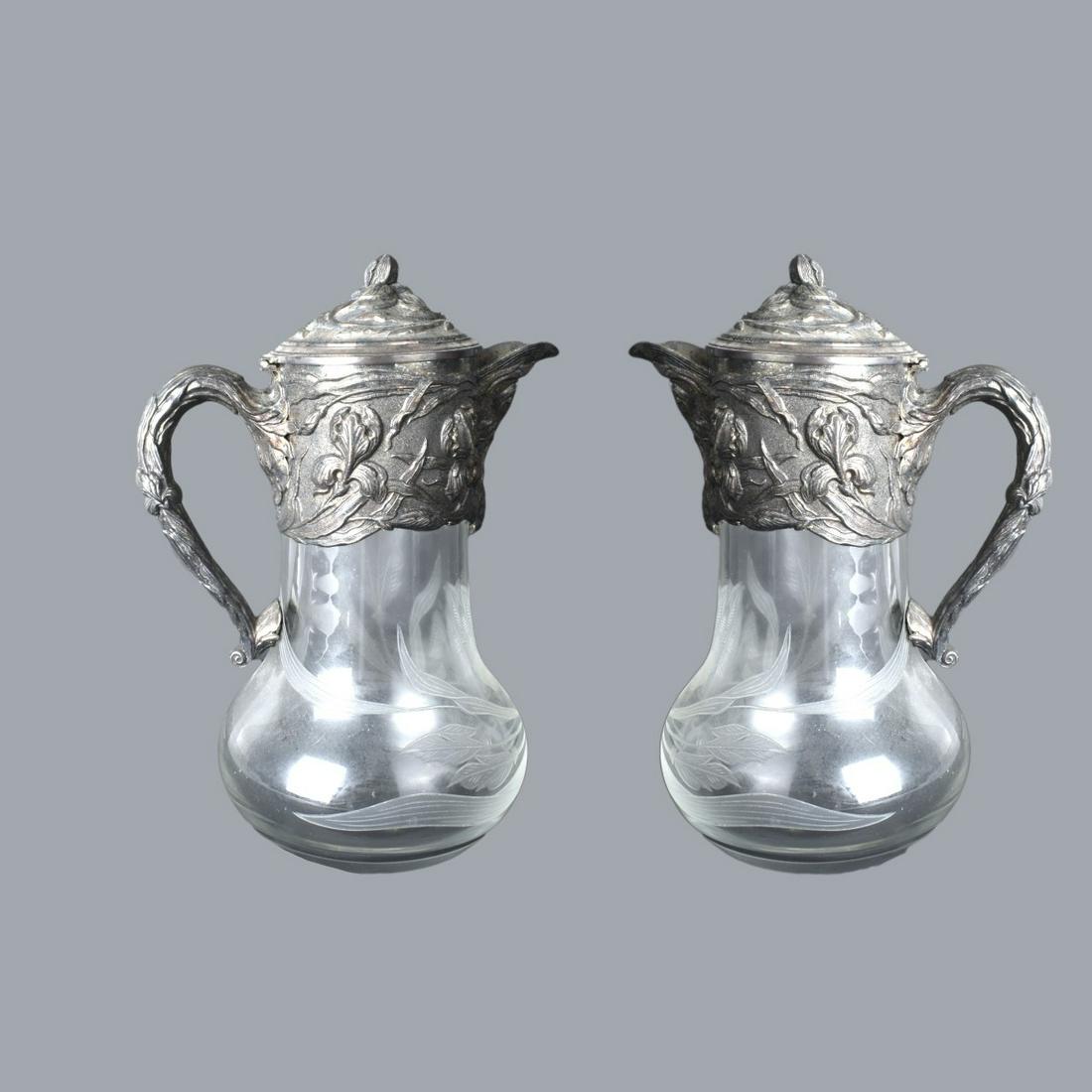 Pair of Art Nouveau Style Ewers: Pair of Art Nouveau Style Etched Glass Ewers with Floral Relief Silverplate Embellishment. Unmarked. Measures 11" x 7-1/2" x 5-3/4'. Estimate: $100.00 - $300.00 Domestic Shipping: $88.00 Condition: Si