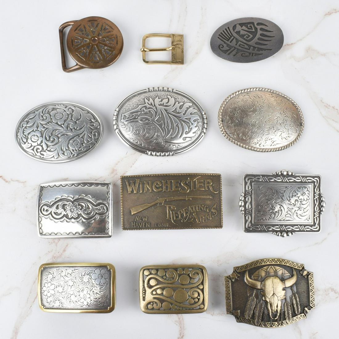 Belt Buckles: Collection of Twelve Men's Belt Buckles. To include brass, white metal, one marked pewter and one marked gold filled. Various makers. Winchester buckle measures 2-1/4" H, 3-7/8" W. Gold filled buckle 