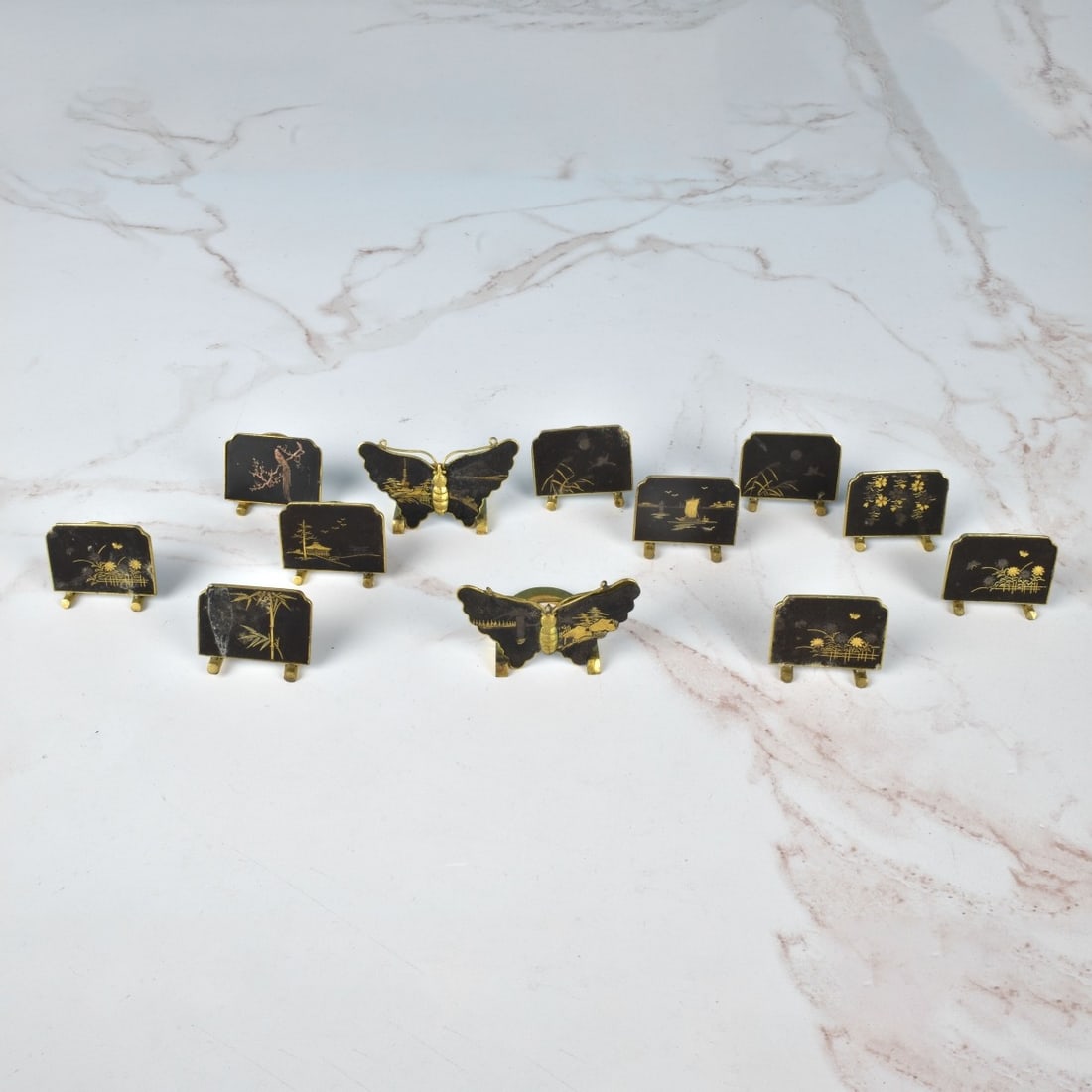 (12) Vintage Japanese Place Card Holders: Grouping of Twelve (12) Vintage Japanese Damascene Place Card Holders. Two are in the shape of a butterfly. Largest measures 1-1/8" x 2" x 1-1/4". Smallest measures 1" x 1-1/4" x 1". Condition: Some s