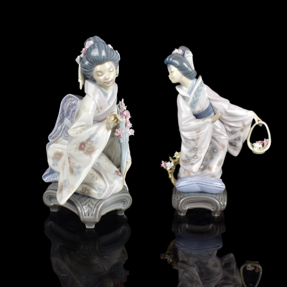 Two Lladro Japanese Lady Figurines: Two (2) Lladro Japanese Lady Figurines with flowers. Kiyoko #01450 sitting, Michiko #1447 basket. Marked to bottom in blue and N23 on one and L17 on other. Tallest measures 8-1/2" H x 6" W. Condition: